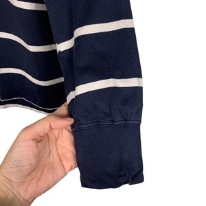 May include: Close-up of a navy blue long-sleeved shirt with horizontal white stripes. The cuff of the sleeve is visible, showing a ribbed texture. The shirt is made of a soft, comfortable material.