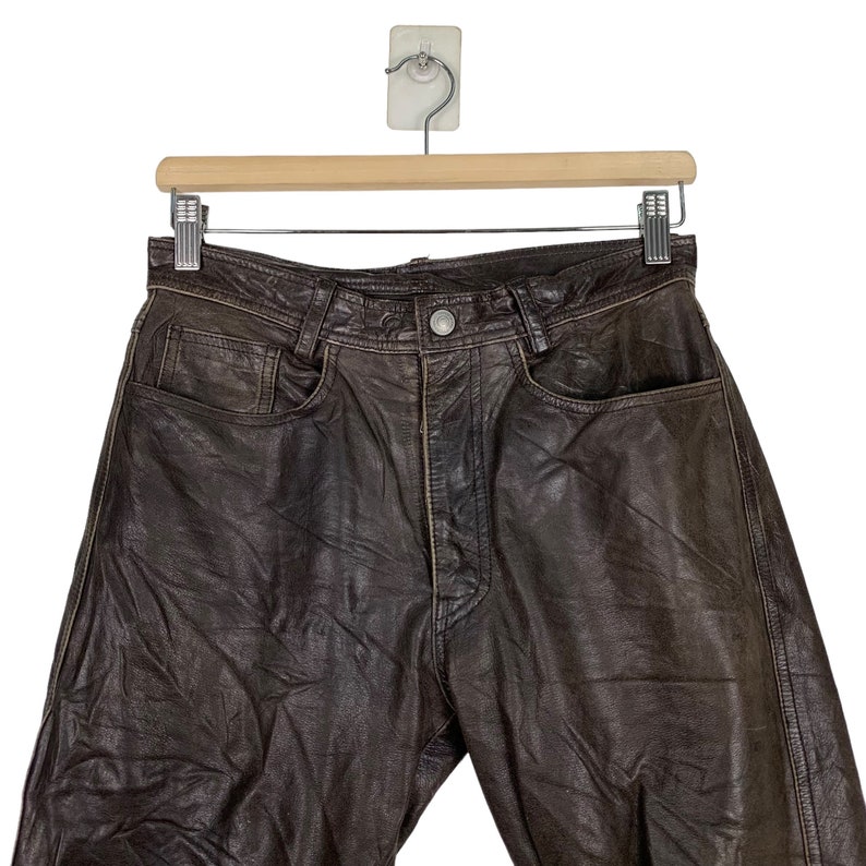 May include: Brown leather pants with a classic five-pocket design. The pants have a button fly and a belt loop waistband.