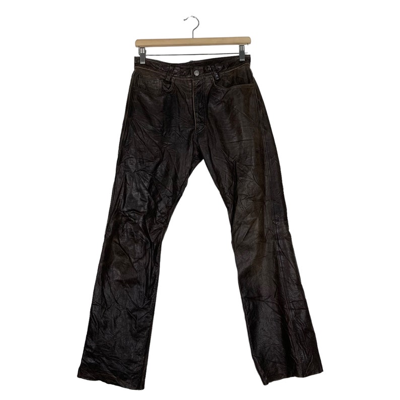May include: Brown leather pants with a straight leg fit. The pants have a button fly and belt loops.