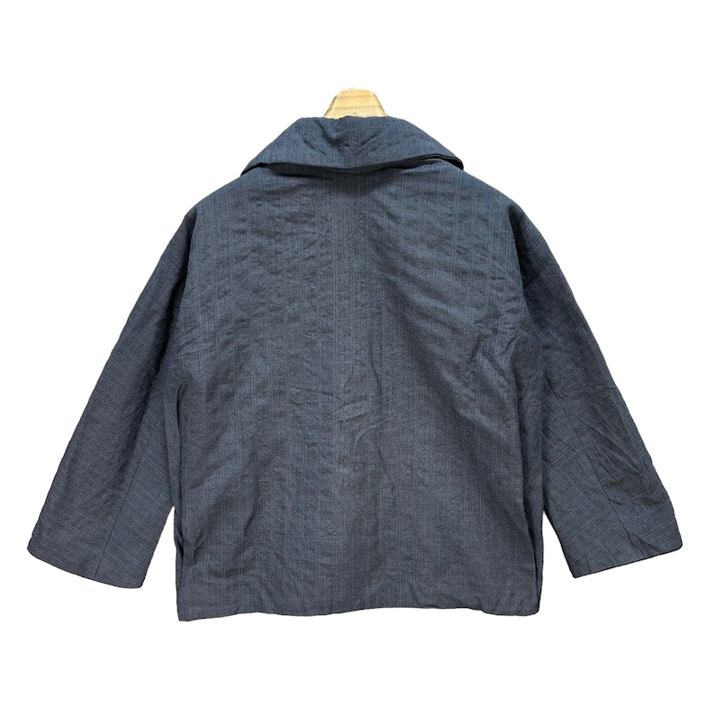 Puede incluir: Una chaqueta de color gris oscuro con rayas finas y cuello y mangas largas.