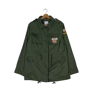 Może przedstawiać: Zielona kurtka typu utility z wieloma kieszeniami i naszywką na lewym rękawie z napisem "Diamond Princess".