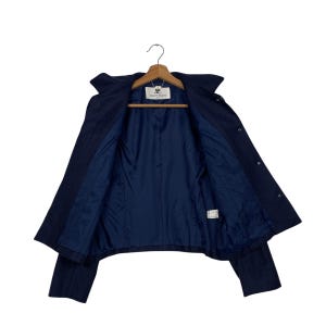 May include: A navy blue jacket with a dark blue interior lining, displayed open on a wooden hanger. The jacket has a classic design with a collar and button closures. The interior lining is a solid, darker shade of blue.