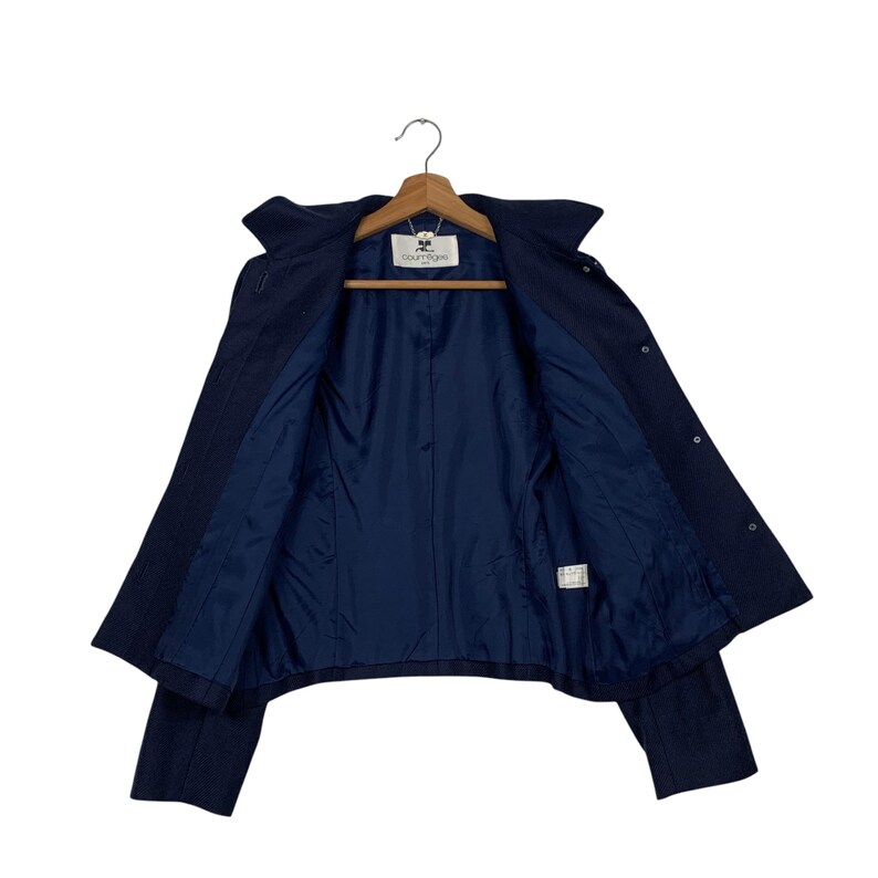 May include: A navy blue jacket with a dark blue interior lining, displayed open on a wooden hanger. The jacket has a classic design with a collar and button closures. The interior lining is a solid, darker shade of blue.