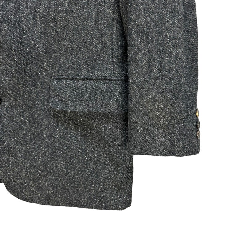 Puede incluir: Una chaqueta gris oscura con un solo bot&oacute;n de cierre y un bolsillo en el lado izquierdo. La chaqueta tiene una tela texturizada y un brillo sutil.