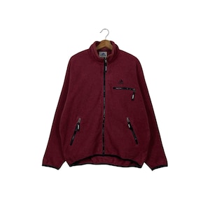 Può includere: Una giacca con zip in pile rosso con tiretti neri e un piccolo logo Adidas sul petto sinistro.
