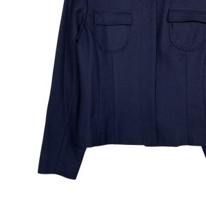 May include: A navy blue blazer with two flap pockets on the chest. The blazer has a textured fabric and a tailored fit. The sleeves are long and the overall design is classic and versatile.
