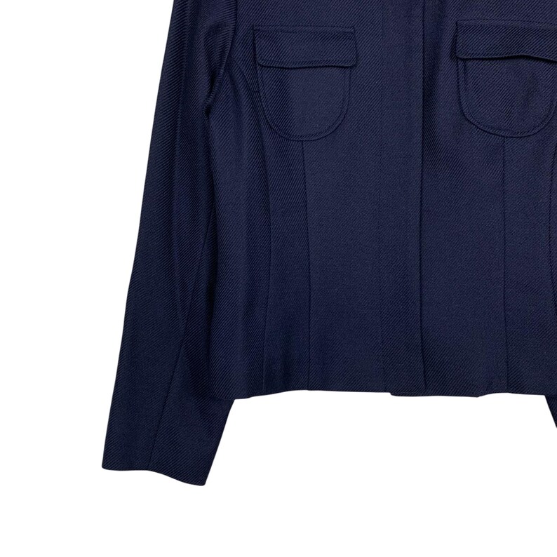 May include: A navy blue blazer with two flap pockets on the chest. The blazer has a textured fabric and a tailored fit. The sleeves are long and the overall design is classic and versatile.