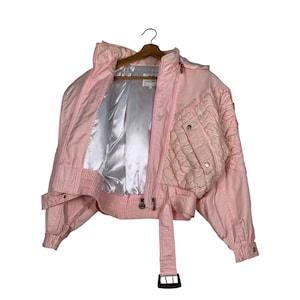 May include: A pink quilted jacket with a zip closure and a belt. The jacket has a satin lining and a quilted design on the front and back.