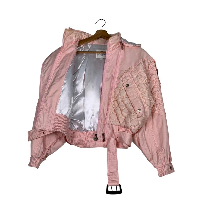 May include: A pink quilted jacket with a zip closure and a belt. The jacket has a satin lining and a quilted design on the front and back.