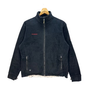 Może przedstawiać: Czarna kurtka polarowa z zamkiem błyskawicznym i napisem "MAMMUT" w kolorze czerwonym z przodu.