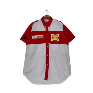 May include: A white and red short-sleeved button-down shirt with a large yellow Shell logo on the front. The shirt also has a smaller yellow "Formula Shell" logo on the left side of the chest.