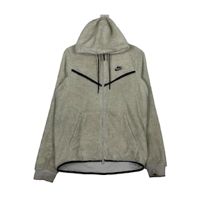 May include: A light gray fleece zip-up hoodie with a black Nike swoosh logo on the chest. The hoodie has a black zipper and a black drawstring hood.