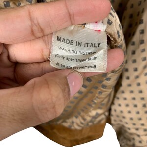 May include: A close-up of a tag that reads "MADE IN ITALY" with washing instructions. The tag is white with black text and is sewn into a tan fabric with a geometric pattern.