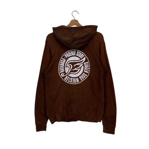 Op de afbeelding: Bruin hoodie met een witte grafische print op de rug. De grafiek toont een cirkel met de tekst "HAYABUSA - PHOENIX STORY - SINGER SONG WRESTLER" en een gestileerde vogelvleugel in de cirkel.