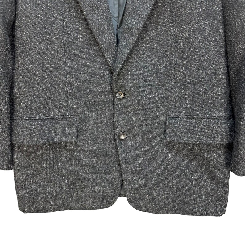 Puede incluir: Una chaqueta gris oscura con tejido texturizado. La chaqueta tiene dos bolsillos y cierre de bot&oacute;n.