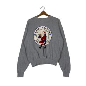 Puede incluir: Sudadera gris con un logotipo circular que presenta a un Papá Noel de dibujos animados sosteniendo un palo de golf y una bolsa de regalo. El logotipo dice "Bobby Barnon Golf Club".