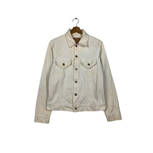 May include: A white denim jacket with a button closure and two chest pockets.
