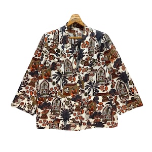 May include: A white button-up shirt with a colorful, intricate pattern of brown, orange, and blue. The pattern features buildings, trees, and people.