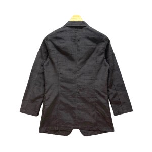Puede incluir: Una chaqueta negra con cierre de un solo bot&oacute;n y mangas largas. La chaqueta est&aacute; hecha de una tela texturizada.