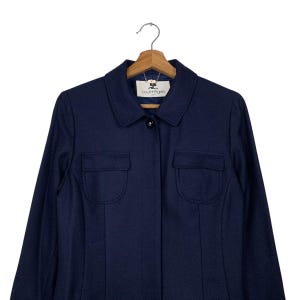 May include: A navy blue jacket with two front pockets and a collared neckline. The jacket is hanging on a wooden hanger. The brand name "courreges" is visible on a label near the collar.