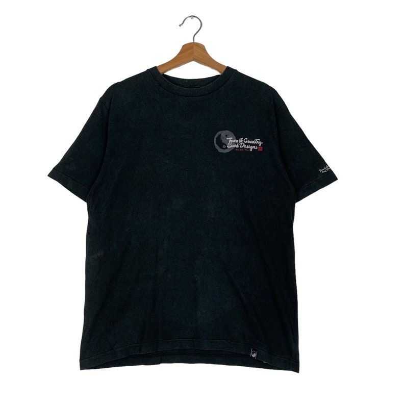 May include: Black short-sleeved t-shirt with a graphic of a yin-yang symbol and the text "Team & Country Surf Designs" in white and red lettering.