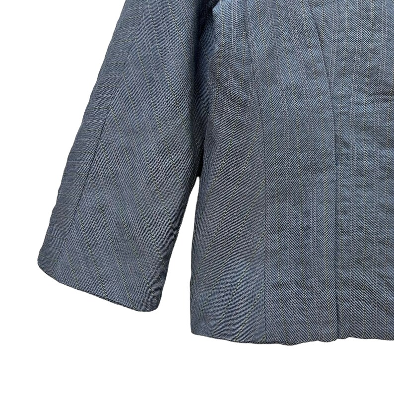 Puede incluir: Una chaqueta azul con un patr&oacute;n de rayas finas. La chaqueta tiene manga larga y un cierre de un solo bot&oacute;n.