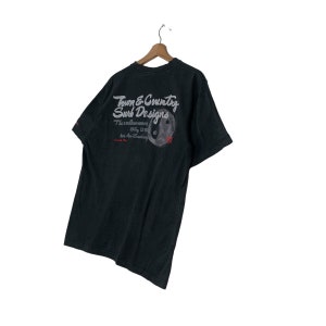 May include: Black t-shirt with a white graphic print of "Town & Country Surf Designs" and a yin yang symbol. The text reads "The endless wave Stay Strong Let the Sun Shine" and "Town & Country".