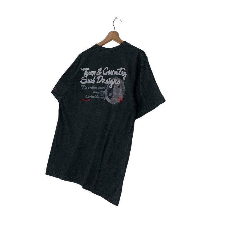 May include: Black t-shirt with a white graphic print of "Town & Country Surf Designs" and a yin yang symbol. The text reads "The endless wave Stay Strong Let the Sun Shine" and "Town & Country".