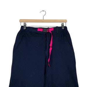May include: Black pants with a pink belt. The pants have two pockets on the front.