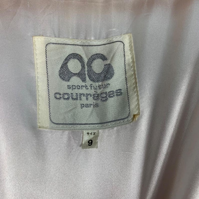 May include: White label with black text that reads "sport futur courr&egrave;ges paris" and a black "ac" logo. The label has a white border and is attached to a white fabric.