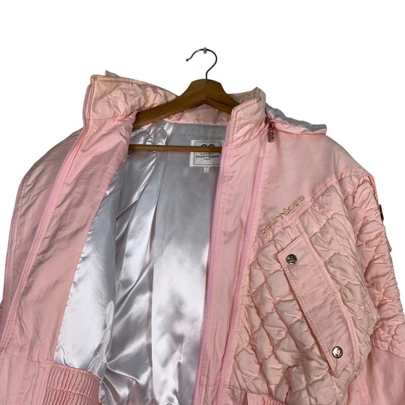 May include: A pink ski jacket with a quilted design and the word "Couragers" embroidered on the front. The jacket has a zip closure and a hood.