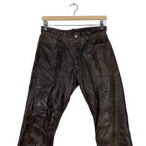 May include: Brown leather pants with a classic five-pocket design. The pants have a straight leg and a relaxed fit.
