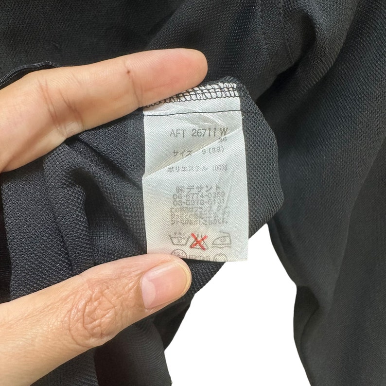 May include: A white tag with black text attached to a black garment. The tag reads "AFT 26711 W 36 Size 9 (38) Polyester 100% Descente 06-6774-0359 03-6979-6101 This product is made in France, Kun."
