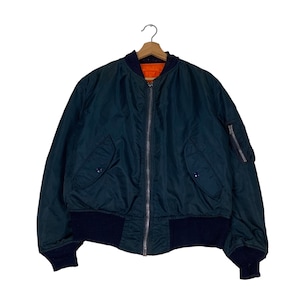 May include: A dark green bomber jacket with a zip closure and a navy blue ribbed collar, cuffs, and waistband. The jacket has two flap pockets on the front and a zipped pocket on the left sleeve.