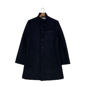 May include: A navy blue wool coat with a button-up front, a small chest pocket, and two side pockets. The coat has a stand-up collar and long sleeves. It is hanging on a wooden hanger.