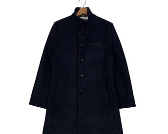 May include: A navy blue wool coat with a button-up front, a small chest pocket, and two side pockets. The coat has a stand-up collar and long sleeves. It is hanging on a wooden hanger.