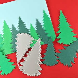 May include: A set of green paper Christmas tree cutouts on a red background. A silver metal die cut of a Christmas tree is also included.