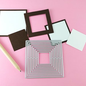 May include: A set of craft supplies for card making, including a pencil, a silver metal die cut of a square with multiple nested squares, and four brown cardstock squares with white cardstock inserts.