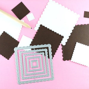 May include: A set of five silver metal square-shaped die-cut frames with scalloped edges. The frames are nested inside each other, with the smallest frame in the center. The frames are on a pink surface.