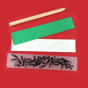 May include: Three embossing plates with a mistletoe design. The plates are green, white, and clear with black ink. A wooden rolling tool is also included.