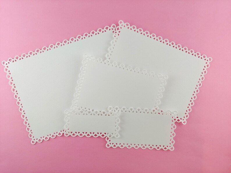 May include: Four white paper doilies with scalloped edges, arranged in a stack, on a pink background.