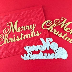 May include: Gold-colored die-cut letters spelling "Merry Christmas" on a red textured background. The image includes a red card and two additional cut-out phrases. Festive holiday decor.