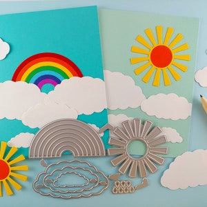 May include: A set of craft dies for creating a rainbow, sun, and clouds. The dies are made of metal and are designed to be used with a die-cutting machine. The dies are shown on a blue background with paper cutouts of the designs.