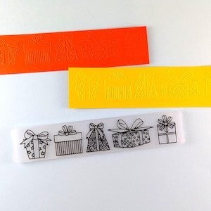 May include: Three rectangular molds with gift box designs. One is orange, one is yellow, and the third is clear with black line art. The molds feature various gift box styles with bows and ribbons.
