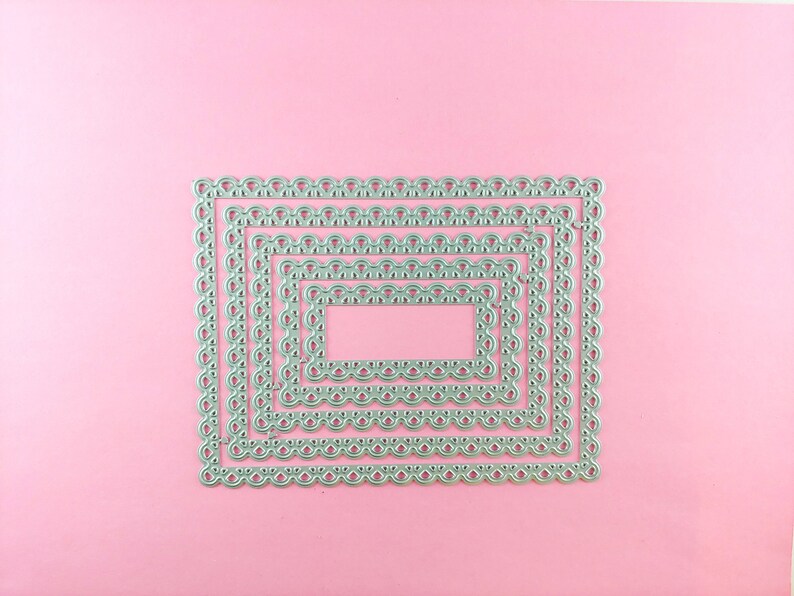 May include: Five silver metal frames with scalloped edges, nested inside each other, on a pink background.