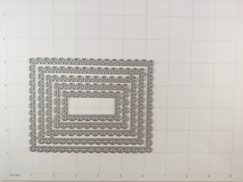May include: Five silver metal rectangle-shaped die-cut frames with a decorative scalloped edge. The frames are nested inside each other, with the largest frame measuring approximately 7 inches by 5 inches.
