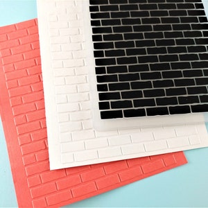 May include: Three brick-patterned embossing folders, one red, one white, and one black. The folders are stacked on top of each other.