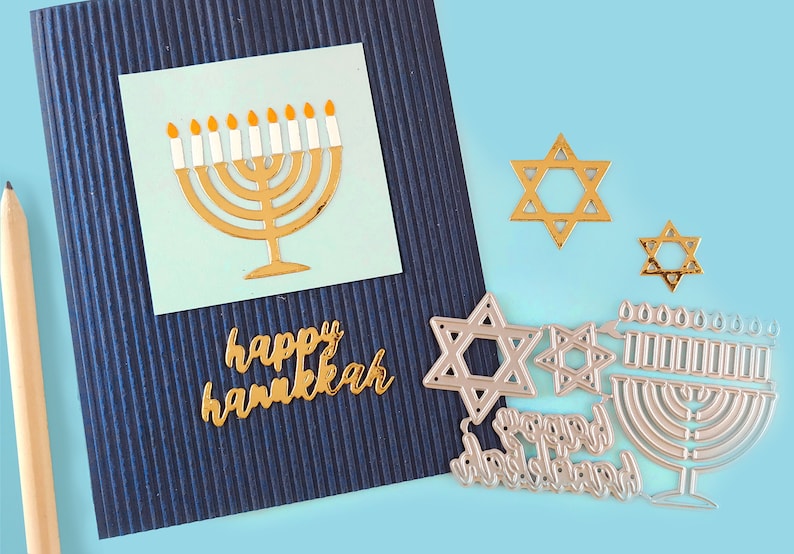 May include: A blue card with a gold menorah and the words "happy hanukkah" on it. There are also gold and silver Star of David cutouts and a silver menorah cutout.