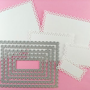 May include: A set of six silver metal die-cut frames with scalloped edges. The frames are arranged in decreasing size, with the largest frame at the top and the smallest frame at the bottom. The frames are on a pink background.
