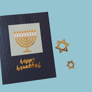 May include: A blue card with a gold menorah and the words "happy hanukkah" on it. There are two gold Star of David stickers on the blue background.